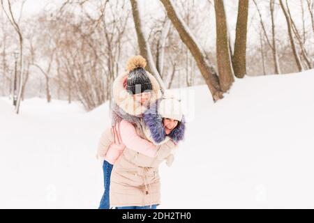 Zwei Mädchen spielen Schneebälle im Winter im Wald. Schwestern in einem warmen Kleid haben Spaß mit Schnee im Winter Stockfoto