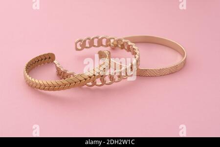 Drei moderne goldene Armbänder auf rosa Hintergrund Stockfoto