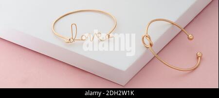 Wort Liebe und Knoten Form goldene Armbänder auf rosa und Weißer Hintergrund mit Kopierbereich Stockfoto