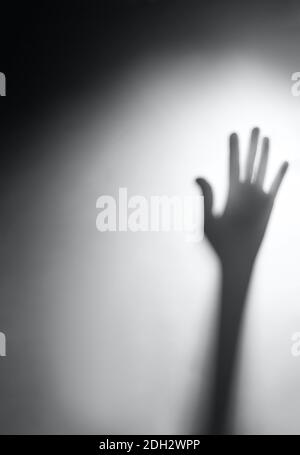 Schatten einer verschwommenen Hand hinter weißem Milchglas, Film. Das Konzept von gefährlich, beängstigend, Hilfe, Horror und Angst. Stockfoto
