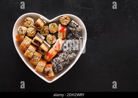 Sushi in Teller als Herz auf schwarzem Hintergrund. Valentinstag Essen Liebe Konzept. Blick von oben. Leerzeichen für Text. Flache Lay-Optik. Stockfoto