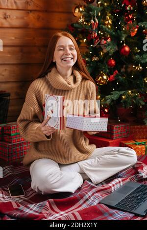 Portrait von fröhlichen jungen Frau Eröffnung Geschenkbox mit Weihnachten Geschenk auf dem Hintergrund des Weihnachtsbaums Stockfoto