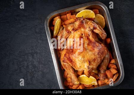 Ganz gebackenes Huhn mit Karotten und Orangen auf schwarzem Hintergrund. Nahaufnahme und Draufsicht Stockfoto