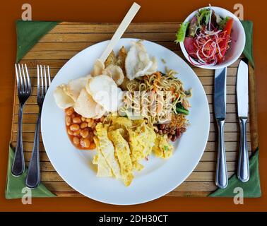 Verschiedene asiatische Speisen Frühstück Einstellung mit einem Teller mit gebratenen Reisnudeln, Krabben Chips, Ei Omelette, Bohnen, zusammen mit einer gemischten Salatschüssel auf einem Bambo Stockfoto