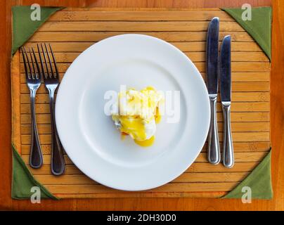 Frühstücksset mit einem überzogenen Ei Benedict und Besteck auf einem Bambustablett Stockfoto