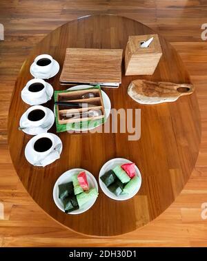 Asiatisches Frühstücksarrangement mit vier Kaffeetassen, Besteck und zwei Tellern mit Obst, Reisetaschen und Eierrollen-Snacks auf einem Bambus-Kaffeetisch. Stockfoto