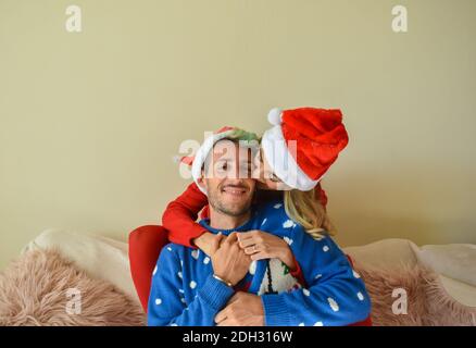 Ein junges glückliches Paar posiert in Weihnachtspullover und Weihnachtsmann Hüte genießen die Urlaubsstimmung Stockfoto