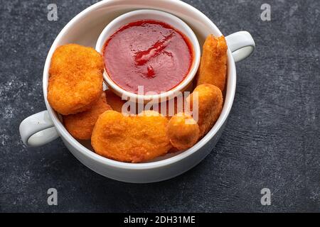 Nuggets in einem weißen tiefen Teller, mit Sauce im Inneren des Tellers, auf dunklem Beton Stockfoto