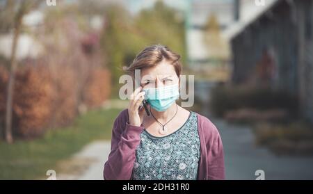 Rauchgas- und Corona-Sicherheitskonzept. Frau trägt Gesichtsmaske, um sich zu schützen und mit Smartphone. Im Freien Stockfoto