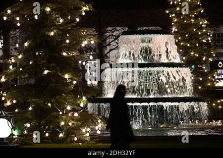 Wiesbaden, Deutschland. Dezember 2020. Abends geht eine Frau über das 'Bowling Green' im Wiesbadener Kurhaus, wo Weihnachtsbäume und ein Kaskadenbrunnen festlich beleuchtet werden. Kredit: Arne Dedert/dpa/Alamy Live Nachrichten Stockfoto