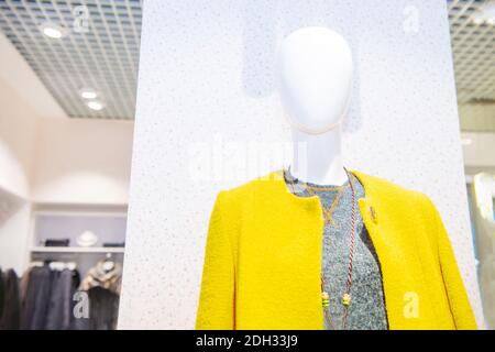 Weibliche Schaufensterpuppe in der leuchtend gelben Mantel und grau oben auf der Vitrine eines Modehauses. Trendige Farben von 2021 in der Shopping Mall. Selektiv Stockfoto