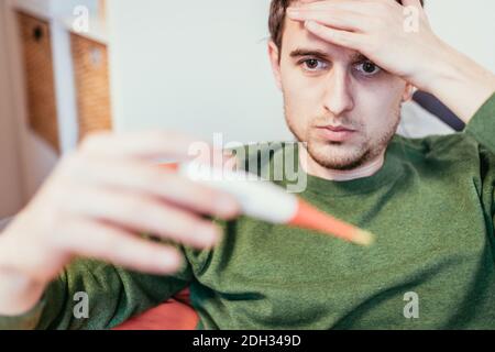 Grippe und Corona Konzept: Der Mensch hält ein Fieberthermometer in der Hand, aus nächster Nähe Stockfoto