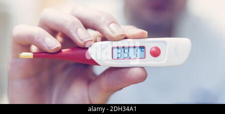 Grippe und Corona Konzept: Der Mensch hält ein Fieberthermometer in der Hand, aus nächster Nähe Stockfoto