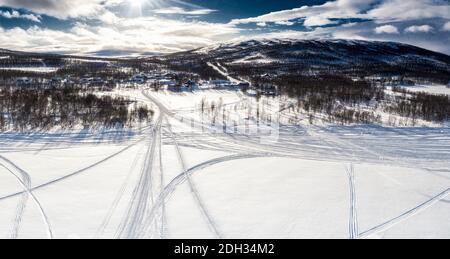 Landschaftlich schöne Luftaufnahme auf Schneemobilstrecken aus verschiedenen Richtungen auf bedeckt von weißem Schnee gefrorenen Bergsee zu kleinen Dorf Joesjo, Schwedisch Lapla Stockfoto