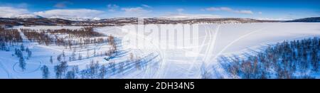 Landschaftlich schöne Luftpanorama auf Schneemobilstrecken von Birkenwald in verschiedene Richtungen auf bedeckt von weißem Schnee gefrorenen Bergsee, Joesjo, Schwedisch L Stockfoto