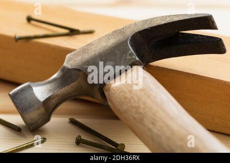 Nahaufnahme eines Hammers, der neben Nägeln auf einer Holzplanke an einem für den Bau vorbereiteten Arbeitsplatz liegt Stockfoto