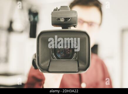 Professionelle Filmproduktion: Männlicher Filmemacher zeichnet mit einer professionellen Filmkamera auf. Nahaufnahme des Kameraobjektivs. Stockfoto