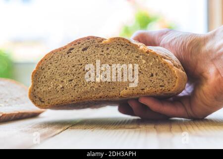 Frisches rustikales Brot am Morgen. Hände des Bäckers mit einem halben Laib Brot Stockfoto