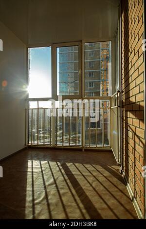 Die helle Sonne scheint wunderschön durch das Fenster auf dem Balkon mit Bars und Kunststofffenstern. Werfen Sie einen Schatten auf eine Ziegelmauer. Stockfoto