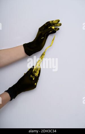 Minimalistischer Hintergrund in trendigen 2021 Farben. Grau und gelb. Hände in Handschuhe mit einem Palettenmesser in gelber Farbe auf grauem Hintergrund. Stockfoto
