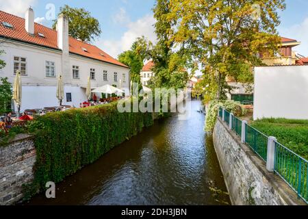 Touristen und Einheimische essen Mittagessen in einem Café im Freien neben einem Kanal direkt an der Moldau in der malerischen Gegend der Kampa Insel in Prag, Tschechische Repub Stockfoto