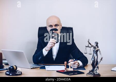 Ein hübscher Notar sitzt am Holztisch und hält als Zeichen von Recht und Ordnung einen Absatz in der Hand. Stockfoto