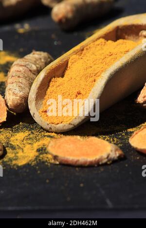 Kurkuma Pulver in einem Holzlöffel und Wurzeln auf einem dunklen Tisch (Curcuma longa), Kurkuma Stockfoto