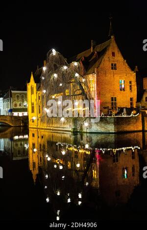 Historisches Stadtzentrum in Brügge bei Nacht, Belgien. Weihnachtliche festliche Dekoration. Alte mittelalterliche Gebäude spiegeln sich im Wasser. Zauberhafte Winterzeit. Stockfoto