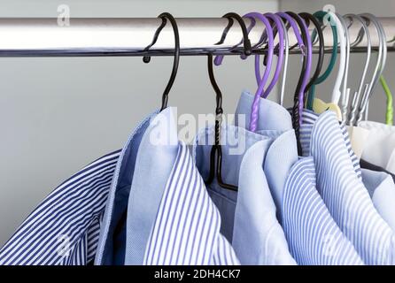 Gruppe von hellblau gestreiften Hemden, die an der Stange einer weißen Garderobe hängen. Herrenmode und klassische Bekleidung. Stockfoto