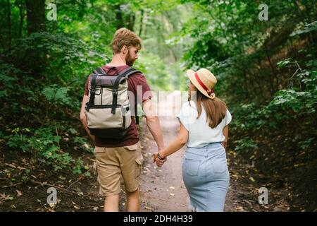 Paar hält Hände im Wald, Rückansicht. Abenteuer, Reisen, Tourismus, Wandern, Menschen. Rückansicht von zwei Personen, die BA tragen Stockfoto