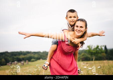 Frau spielt mit kleinen Sohn auf dem Feld mit Unkraut und Wiesenblumen am Sommertag. Sorglose Mutter Spaß mit Kind auf sho Stockfoto