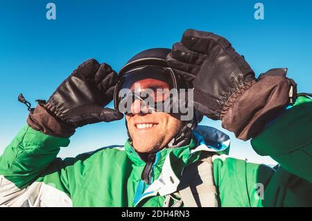 Lächelnder Skifahrer oder Snowboarder Mann Porträt in sicheren Skihelm und Brille mit blauem Himmel Hintergrund. Aktive Menschen oder aktive Ferien Konzeptbild. Stockfoto