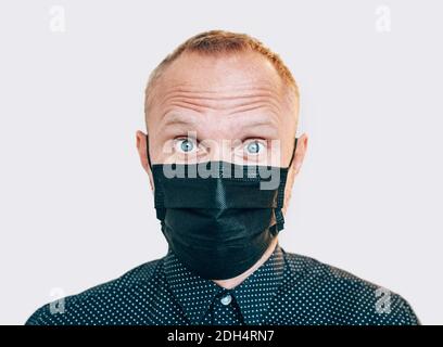 Porträt eines überraschten Mannes in schwarzer Gesichtsmaske während einer COVID-19-Weltpandemie beim Blick auf die Kamera. Selbstschutz und Einhalt der Virusverbreitung c Stockfoto