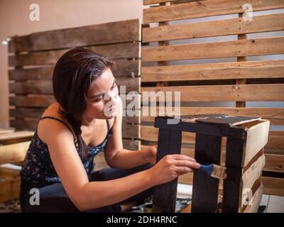 Junge lächelnde hispanische Frau in dunklen Kleidern Farben gekleidet Holzkiste in Schwarz Stockfoto