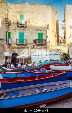 Giovinazzo, Italien: Bunte alte hölzerne Fischerboote, die im Hafen in der Altstadt festgemacht sind; der Platz vor dem Restaurant im Verteidigungsturm Stockfoto