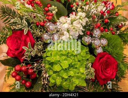 Blumenarrangement in Weihnachtsfarben mit roten Rosen, grünen Hortensien, Stechbeeren und silbernen Glocken. Stockfoto