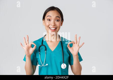 Mitarbeiter im Gesundheitswesen, Virenprävention, Quarantänekampagne Konzept. Aufgeregt und zufrieden asiatische weibliche Arzt, Krankenschwester in Scrubs mit Stockfoto