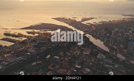 Sonnenuntergang an der Meeresbucht mit Stadt am Flussufer aus der Luft. Beleuchtete Stadtlandschaft mit Straßen und Straßen. Filmkulisse bei Sommersonne unterging Licht. Moderne Architektur Wahrzeichen der Stadt Manila, Philippinen. Stockfoto