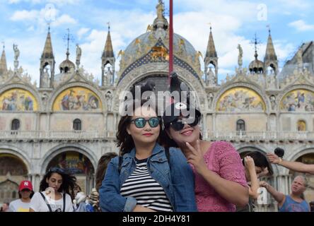 KEINE WEB/KEINE APPS - Asiatische Touristen spielen mit Tauben auf dem Markusplatz, dem Zentrum der touristischen Schwerkraft in Venedig, Italien am 12. August 2017. Tauben füttern ist gegen das Gesetz. Die Stadt Venedig, die von Touristen überfallen wird, riskiert, ‘D„Inselland am Meer“ zu werden. Die meisten Venezianer verachten die giganten Kreuzfahrtschiffe, die jeden Tag durch den Giudecca-Kanal schaufeln, Dämpfe aussenden, die zu Erosion des Watts und Sedimentverlust führen, bevor sie Tausende von Menschen in das historische Zentrum verschleppen. Ob durch Selfie-Stöcke, laute Wheelie-Koffer oder Leute, die auf einer der 391 Brücken schnüffeln, Ve Stockfoto