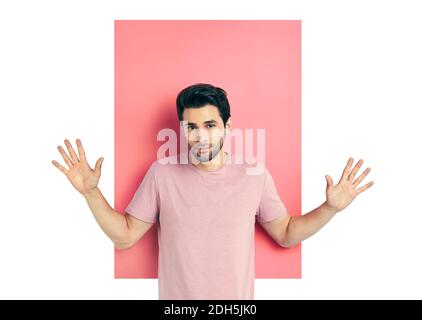 Überrascht junger Mann mit den Armen nach oben in der Kamera über rosa und weißen Hintergrund erstaunt schauen. Stockfoto
