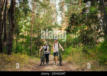 Junge kaukasische Radfahrer gehen und schieben ihre Mountainbikes entlang der Waldstraße im Park. Aktives Sportwochenende. Stockfoto