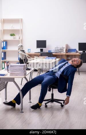 Junger männlicher Angestellter mit Skeletten im Büro Stockfoto