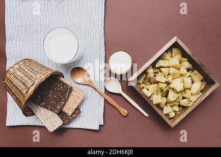 Köstliche Kartoffeln mit Dill auf einem Holzteller gebraten, Salz, verschiedene Brote und Milch. Tabellenansicht von oben. Mittagessen auf dem Land. Stockfoto