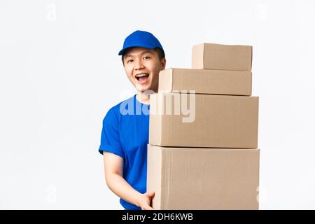 Online-Shopping, schnelles Versandkonzept. Freundlich lächelnd junge asiatische männliche Kurier in blauer Uniform tragen Boxen mit Bestellungen. Lieferg Stockfoto