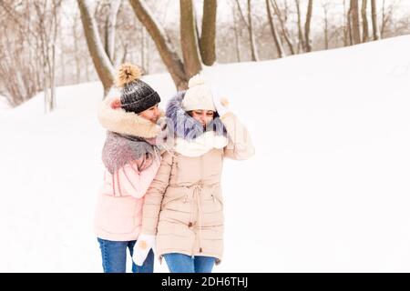 Zwei Mädchen spielen Schneebälle im Winter im Wald. Schwestern in einem warmen Kleid haben Spaß mit Schnee im Winter Stockfoto