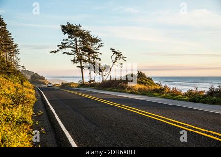 Ein Auto, das auf dem Highway 101 entlang der Küste der Olympischen Halbinsel nach Süden fährt, während die Sonne über dem Pazifik, Washington, USA, untergeht. Stockfoto