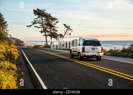 Ein Auto, das auf dem Highway 101 entlang der Küste der Olympischen Halbinsel nach Süden fährt, während die Sonne über dem Pazifik, Washington, USA, untergeht. Stockfoto