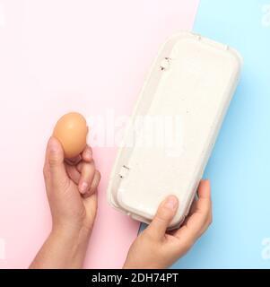 Halten Sie das ganze braune Hühnereichen und das Papiertablett mit der Hand fest Ein rosa Hintergrund Stockfoto
