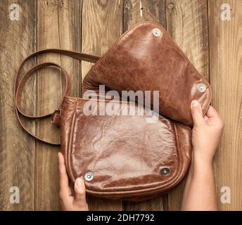 Zwei weibliche Hände halten eine braune Ledertasche an einem Grauer Holzhintergrund Stockfoto