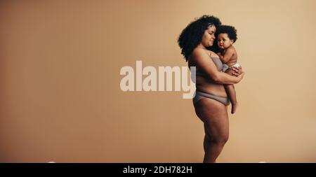 afroamerikanische Frau, die ihr Kind im Studio auf den Armen trägt. Fürsorgliche Mutter mit ihrem Baby. Stockfoto